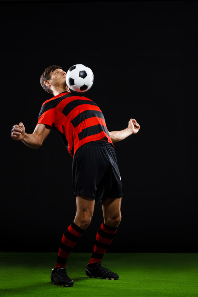 Soccer player in black and red uniform kicking ball on grass over black background