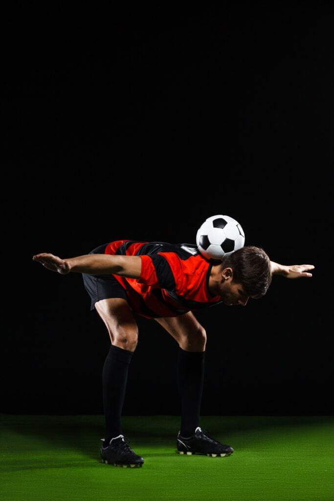 Soccer player in black and red uniform making trick with ball over black background